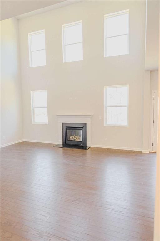 unfurnished living room with a high ceiling, baseboards, wood finished floors, and a glass covered fireplace