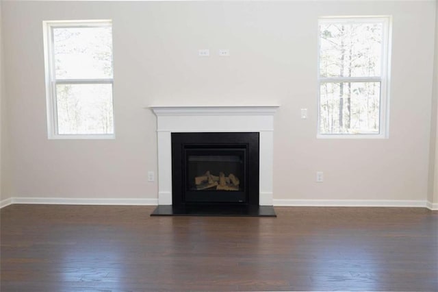 unfurnished living room featuring a glass covered fireplace, baseboards, and wood finished floors