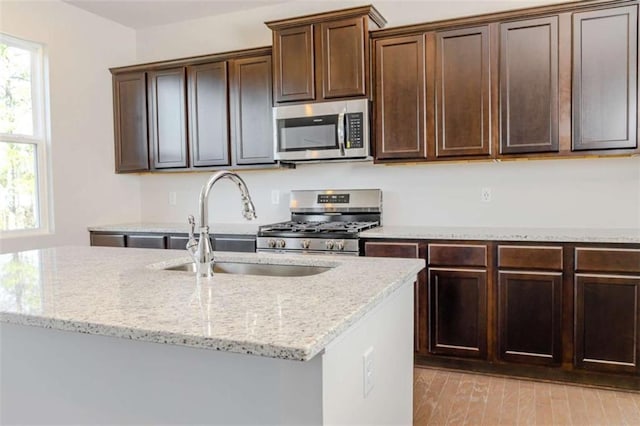 kitchen with appliances with stainless steel finishes, light stone countertops, dark brown cabinets, light wood-style floors, and a sink