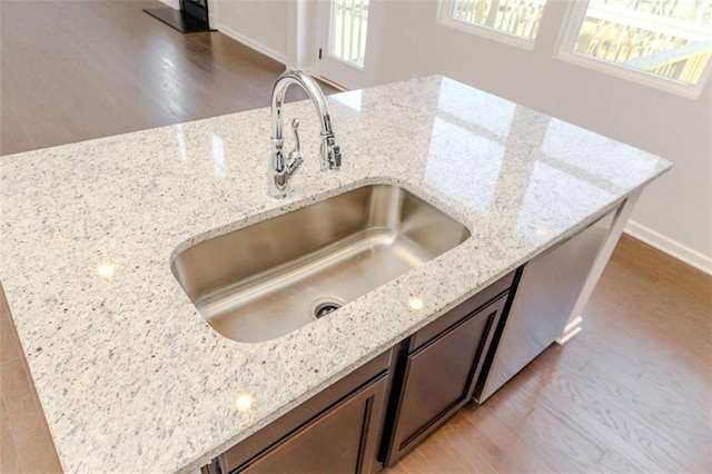 room details featuring baseboards, light wood-type flooring, a sink, and light stone countertops