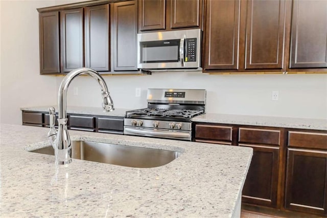 kitchen with dark brown cabinets, appliances with stainless steel finishes, a sink, and light stone counters