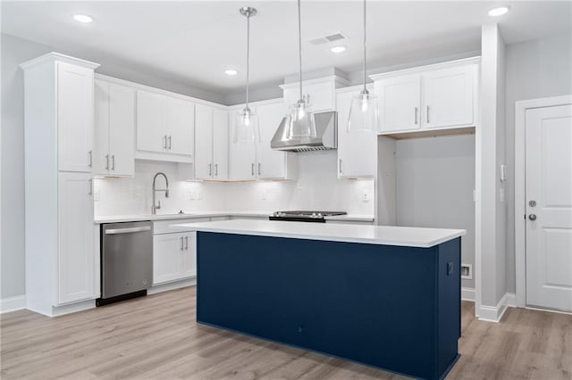 kitchen with appliances with stainless steel finishes, pendant lighting, light countertops, and wall chimney range hood