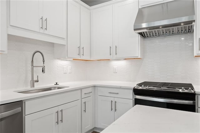 kitchen featuring decorative backsplash, appliances with stainless steel finishes, wall chimney range hood, white cabinetry, and a sink