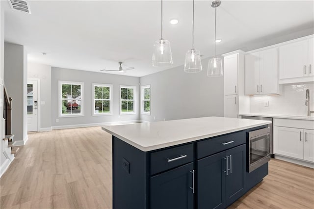 kitchen featuring white cabinets, stainless steel microwave, open floor plan, a center island, and light countertops