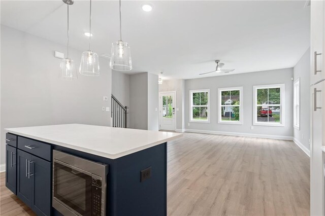 kitchen with open floor plan, light countertops, a center island, stainless steel microwave, and pendant lighting