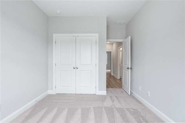 unfurnished bedroom featuring baseboards, a closet, and light colored carpet