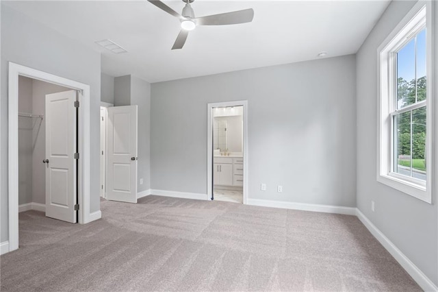 unfurnished bedroom with light carpet, multiple windows, baseboards, and a walk in closet