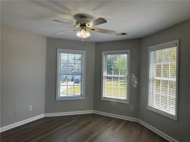 spare room featuring visible vents, a ceiling fan, baseboards, and dark wood-style floors