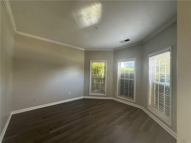 empty room featuring baseboards, visible vents, ornamental molding, and dark wood finished floors