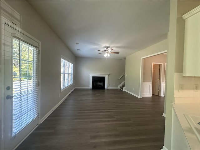 unfurnished living room with ceiling fan, a fireplace, dark wood finished floors, stairway, and baseboards