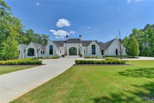 french country inspired facade featuring curved driveway, a chimney, and a front lawn