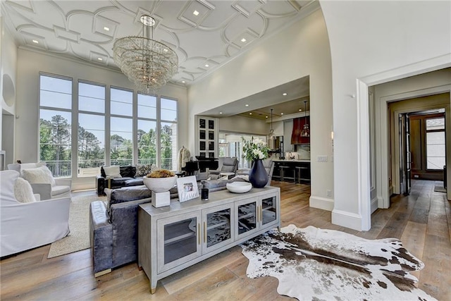 living area featuring crown molding, baseboards, a chandelier, a high ceiling, and light wood-style flooring