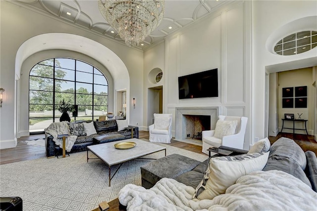 living area with crown molding, a fireplace with flush hearth, a towering ceiling, and wood finished floors