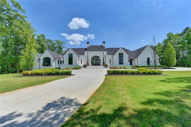 french country inspired facade featuring a chimney, concrete driveway, and a front lawn