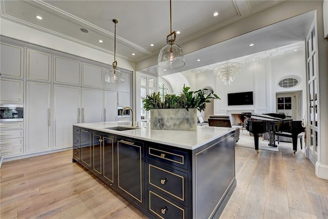 kitchen with pendant lighting, a sink, light countertops, light wood-style flooring, and an island with sink