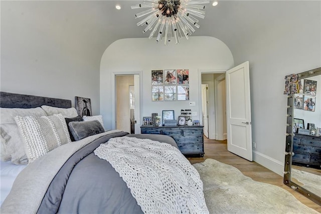 bedroom featuring baseboards, vaulted ceiling, wood finished floors, and a notable chandelier