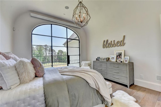 bedroom with baseboards, an inviting chandelier, visible vents, and light wood-style floors