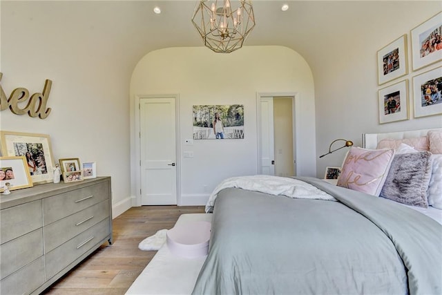 bedroom featuring arched walkways, wood finished floors, baseboards, lofted ceiling, and an inviting chandelier