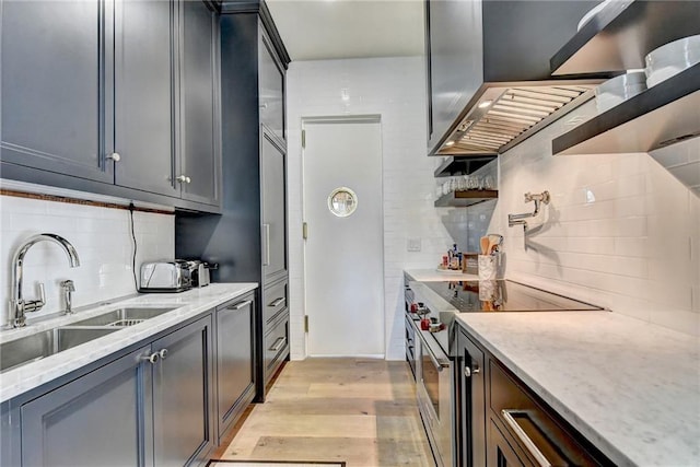 kitchen with decorative backsplash, stainless steel electric range oven, light stone countertops, light wood-type flooring, and a sink