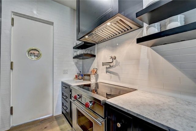 kitchen with light stone counters, dark cabinetry, light wood-type flooring, tasteful backsplash, and high end stainless steel range oven