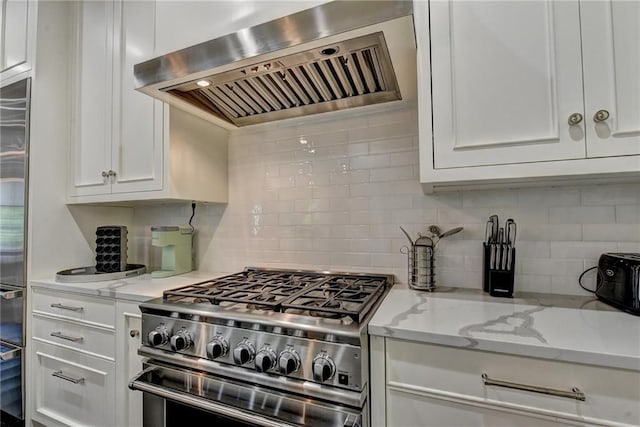 kitchen with wall chimney range hood, light stone countertops, high end range, white cabinetry, and decorative backsplash