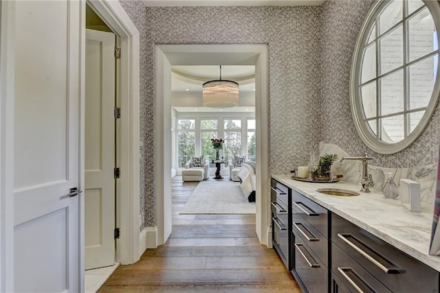 interior space featuring vanity, ensuite bathroom, wallpapered walls, and wood finished floors