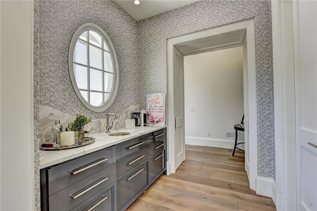 bar with a sink, light wood-style floors, and wallpapered walls