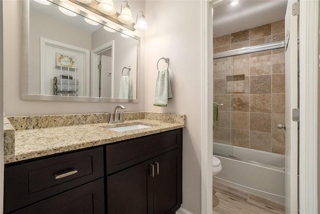 full bathroom with shower / bath combination with glass door, hardwood / wood-style flooring, vanity, and toilet