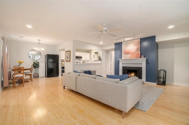 living room featuring ceiling fan with notable chandelier, light hardwood / wood-style floors, and rail lighting