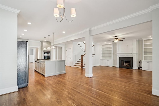 kitchen with wood finished floors, stainless steel appliances, a fireplace, crown molding, and hanging light fixtures