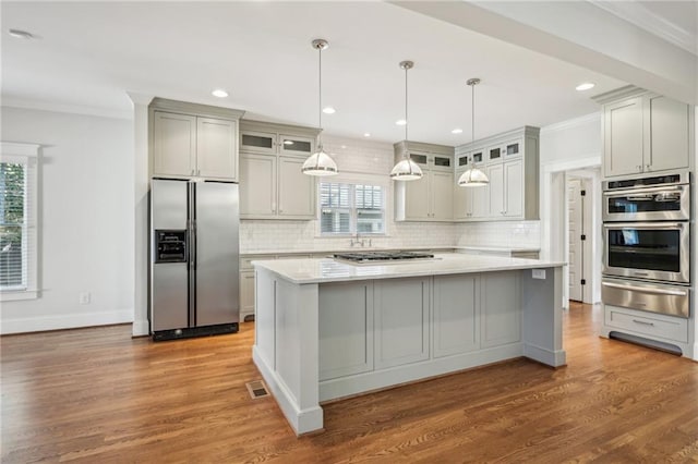 kitchen with a warming drawer, backsplash, wood finished floors, appliances with stainless steel finishes, and light countertops