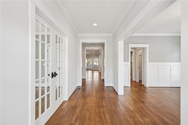 corridor featuring crown molding, wainscoting, french doors, wood finished floors, and a decorative wall