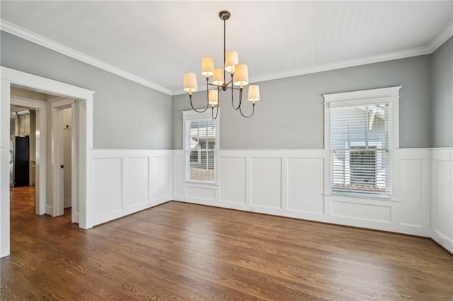 unfurnished dining area featuring an inviting chandelier, wood finished floors, wainscoting, and ornamental molding