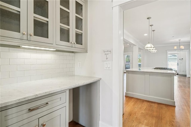 kitchen featuring tasteful backsplash, crown molding, light wood finished floors, glass insert cabinets, and light stone countertops