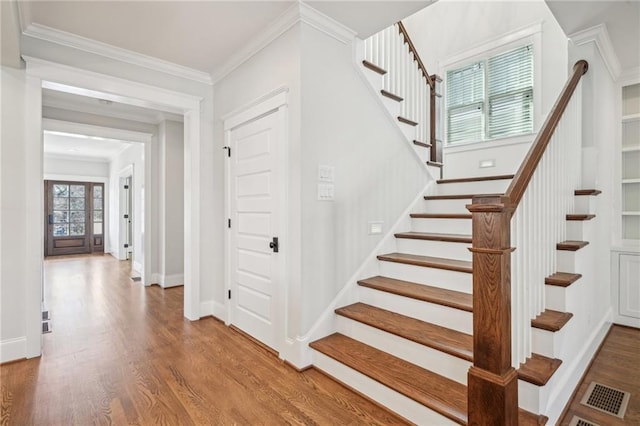 stairs featuring baseboards, wood finished floors, visible vents, and ornamental molding