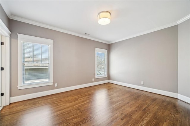 empty room featuring visible vents, ornamental molding, baseboards, and wood finished floors