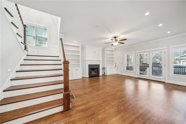 unfurnished living room featuring a fireplace, stairway, wood finished floors, and ornamental molding