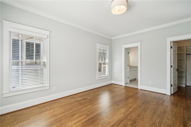 unfurnished bedroom with a spacious closet, crown molding, baseboards, and wood finished floors