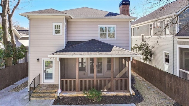 rear view of house with a shingled roof, a fenced backyard, a chimney, and a sunroom