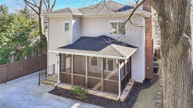 rear view of house featuring central AC unit, fence, roof with shingles, and a sunroom