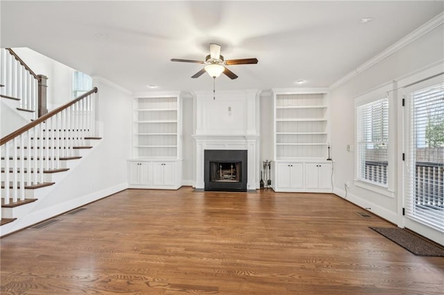 unfurnished living room with built in features, wood finished floors, a large fireplace, crown molding, and baseboards