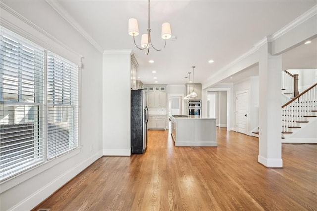 kitchen featuring light wood-style flooring, appliances with stainless steel finishes, glass insert cabinets, and ornamental molding