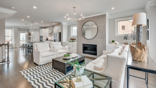 living room featuring dark hardwood / wood-style flooring, an inviting chandelier, a fireplace, sink, and crown molding