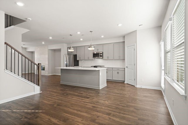 kitchen with decorative light fixtures, gray cabinetry, dark hardwood / wood-style floors, a center island with sink, and stainless steel appliances