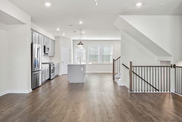 kitchen featuring appliances with stainless steel finishes, decorative light fixtures, sink, dark wood-type flooring, and a kitchen island