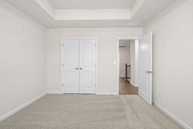 unfurnished bedroom with carpet floors, a closet, and a raised ceiling