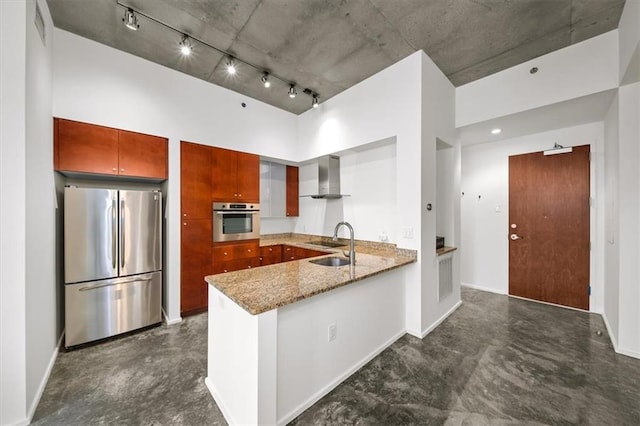 kitchen featuring appliances with stainless steel finishes, sink, light stone counters, kitchen peninsula, and wall chimney range hood