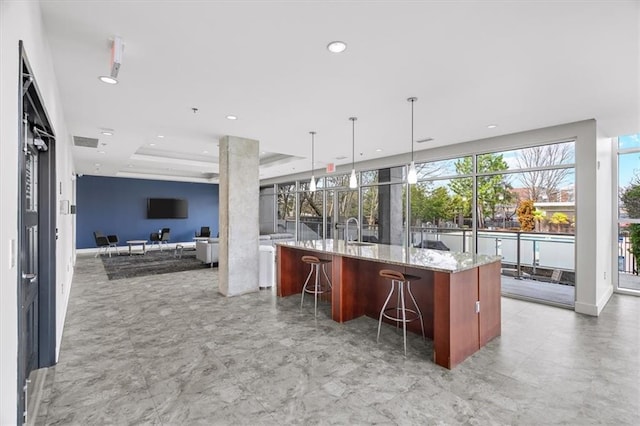 kitchen with decorative light fixtures, light stone countertops, a kitchen island with sink, and a breakfast bar area