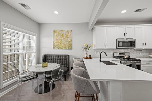 kitchen with sink, appliances with stainless steel finishes, white cabinetry, a kitchen breakfast bar, and kitchen peninsula