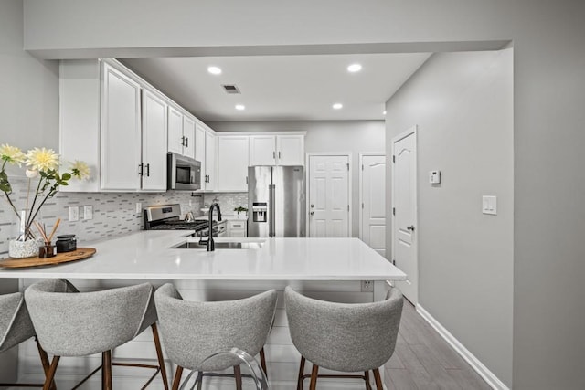 kitchen featuring a kitchen breakfast bar, kitchen peninsula, white cabinets, and appliances with stainless steel finishes